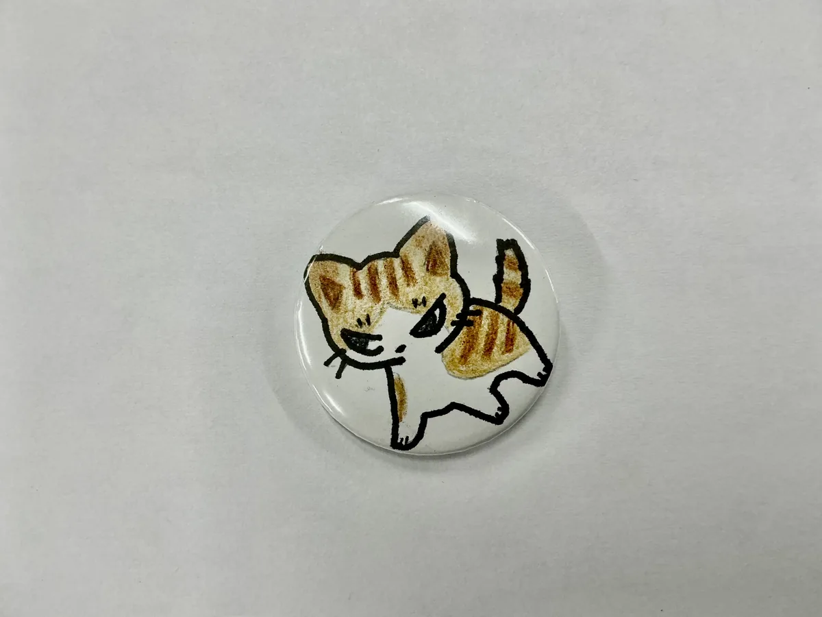 デザインを描いた用紙と缶バッジ
